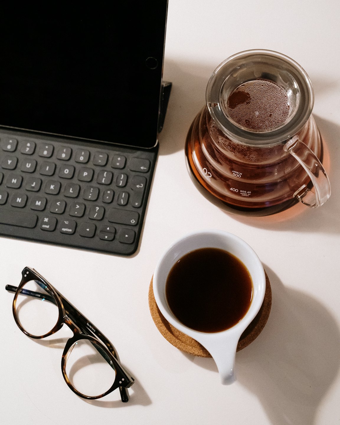 A tablet with keyboard, coffee, and eyeglasses on a desk.