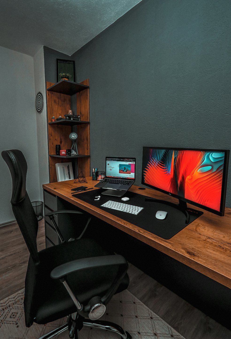 Laptop and monitor on a desk with an ergonomic office chair.